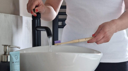 A person holding a bamboo toothbrush under a tab of running water.