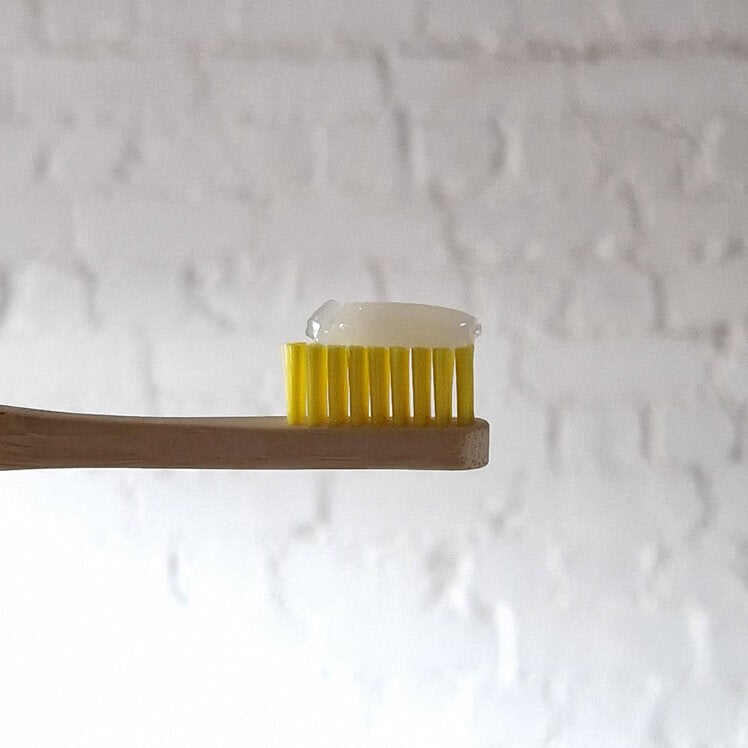 A bamboo toothbrush head with yellow bristles with toothpaste.
